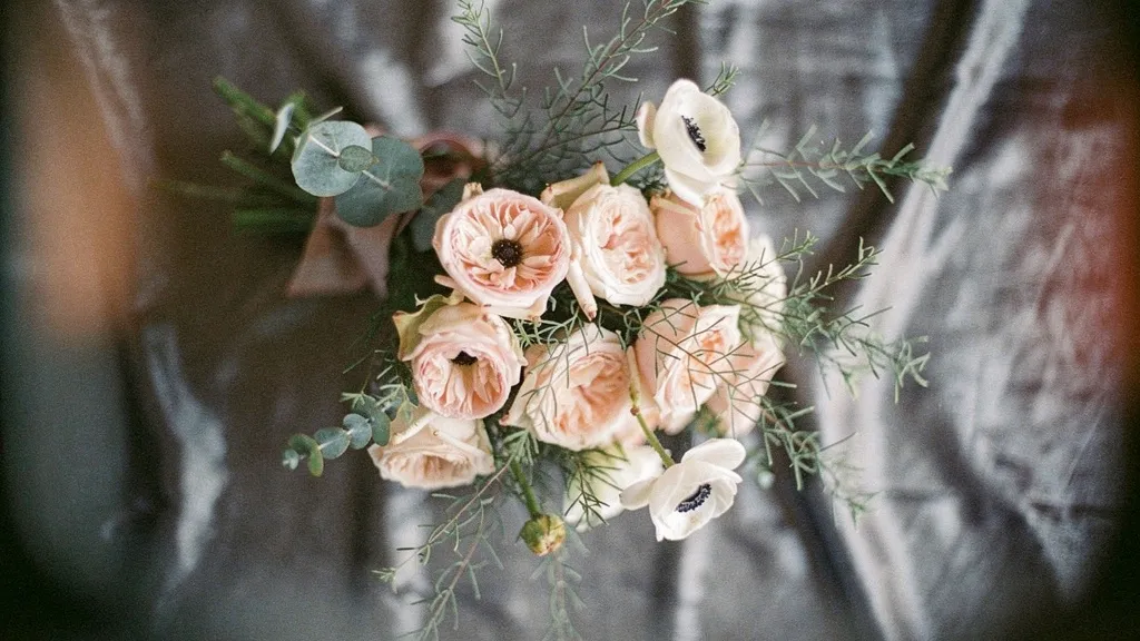 A bouquet detail featuring blush garden roses, white anemones, and eucalyptus sprigs on a pewter gray linen backdrop.